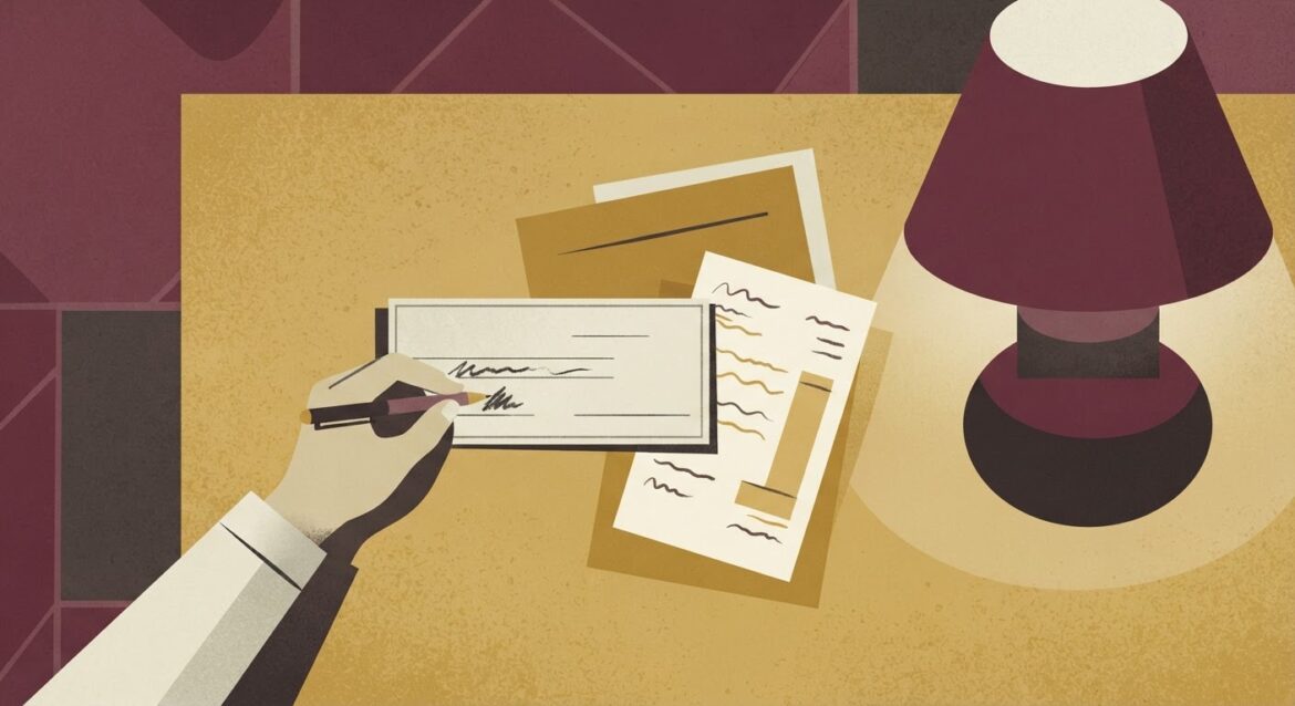 A hand writing a check at a kitchen table next to a rural electric co-op bill and a lamp